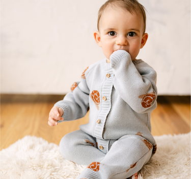 Image shows baby boy wearing organic cotton knit romper with snail jacquard pattern in pearl blue. 