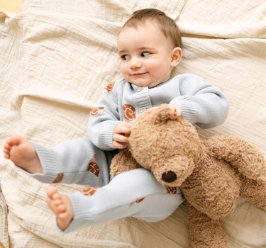 Image shows baby boy wearing organic cotton knit romper with snail jacquard pattern in pearl blue. 