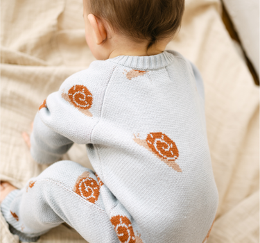 Image shows baby boy wearing organic cotton knit romper with snail jacquard pattern in pearl blue. 