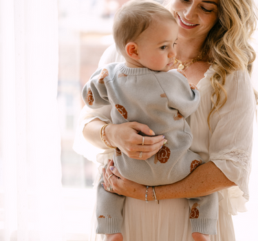 Image shows baby boy wearing organic cotton knit romper with snail jacquard pattern in pearl blue. 