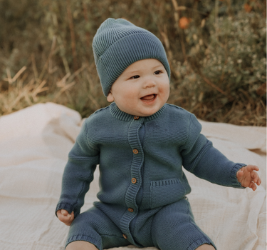 Baby boy wearing organic cotton knit romper with magnetic closures in bluestone.