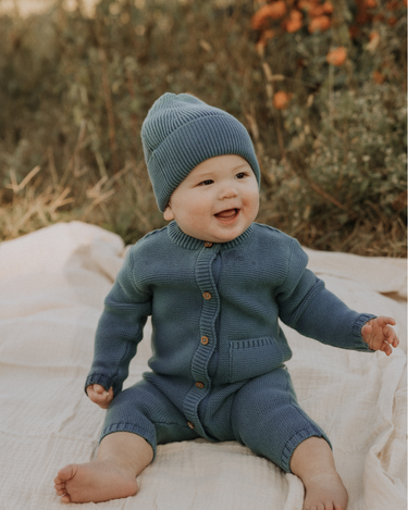 Baby boy wearing organic cotton knit romper with magnetic closures in bluestone.