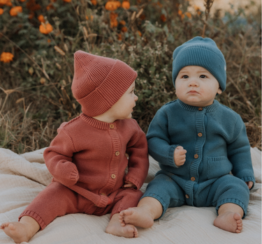 Baby boy wearing organic cotton knit romper with magnetic closures in bluestone.