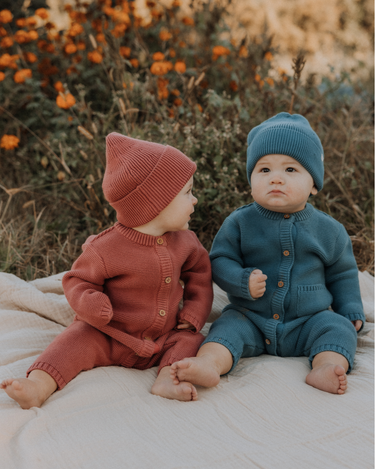 Baby boy wearing organic cotton knit romper with magnetic closures in bluestone.