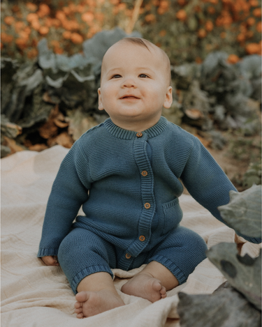 Baby boy wearing organic cotton knit romper with magnetic closures in bluestone.