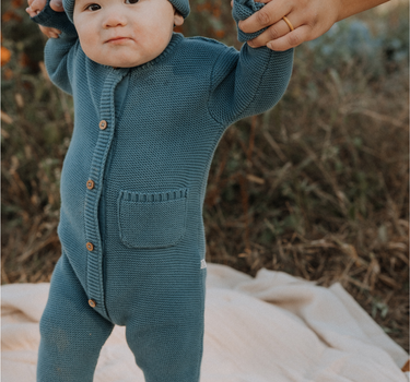 Baby boy wearing organic cotton knit romper with magnetic closures in bluestone.