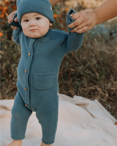 Baby boy wearing organic cotton knit romper with magnetic closures in bluestone.