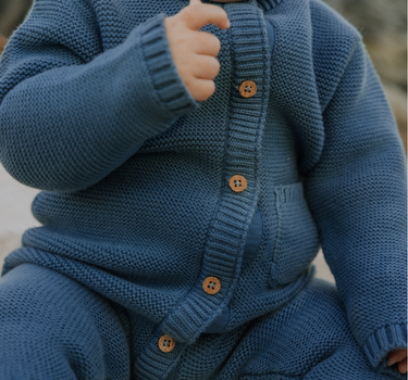 Baby boy wearing organic cotton knit romper with magnetic closures in bluestone.
