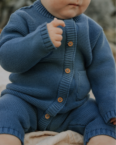 Baby boy wearing organic cotton knit romper with magnetic closures in bluestone.