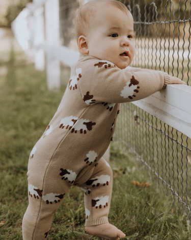 baby wearing organic cotton beige romper with sheep jacquard pattern and magnetic buttons from neck to crotch