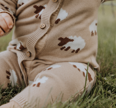 baby wearing organic cotton beige romper with sheep jacquard pattern and magnetic buttons from neck to crotch