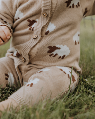 baby wearing organic cotton beige romper with sheep jacquard pattern and magnetic buttons from neck to crotch