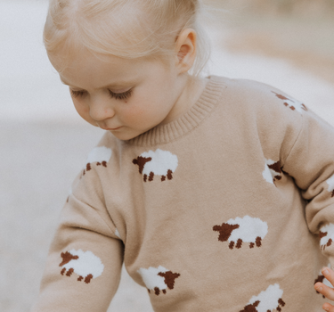 little girl wearing organic cotton beige sweater with sheep jacquard pattern