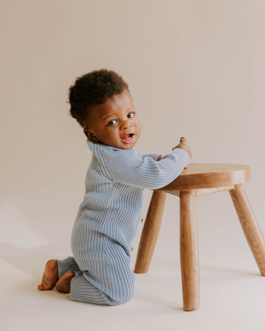 Baby boy kneeling wearing organic cotton rib knit romper with Magnetic Buttons for easy changes in stormy blue color.