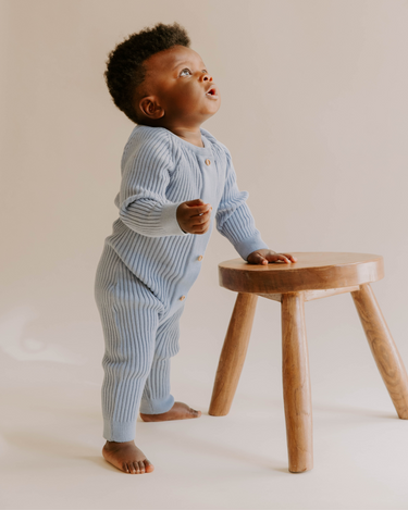 Baby boy standing wearing stormy blue organic cotton rib knit romper with Magnetic Buttons for easy changes.