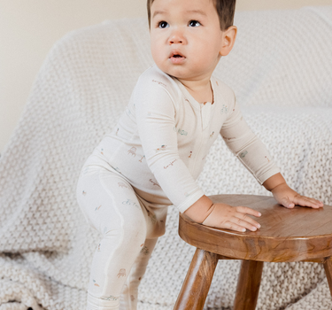 photo shows baby boy leaning on stool wearing modal footy pajamas in Paris print