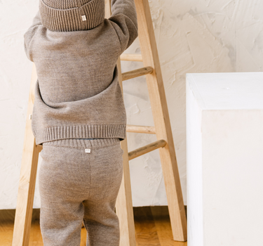 Image shows baby boy wearing merino wool baby gift set in heather brown. 