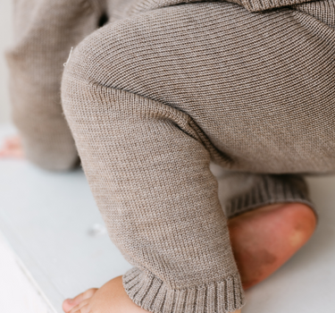 Image shows baby boy wearing merino wool baby gift set in heather brown. 