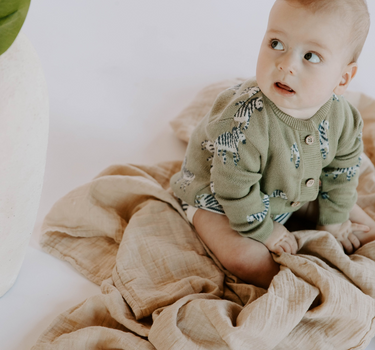 Baby boy wearing organic cotton knit cardigan in sage green with jacquard zebra pattern and magnetic button closures.