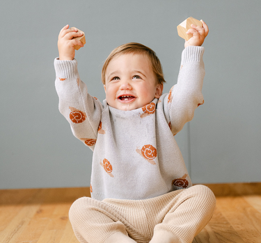 Image shows baby boy wearing organic cotton knit sweater with jacquard snail pattern in pearl blue. 