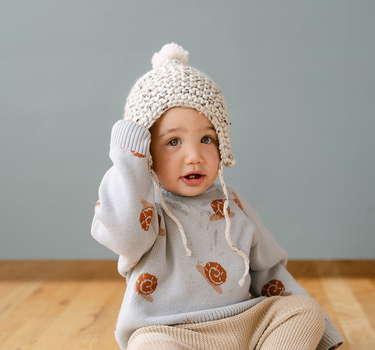 Image shows baby boy wearing organic cotton knit sweater with jacquard snail pattern in pearl blue. 