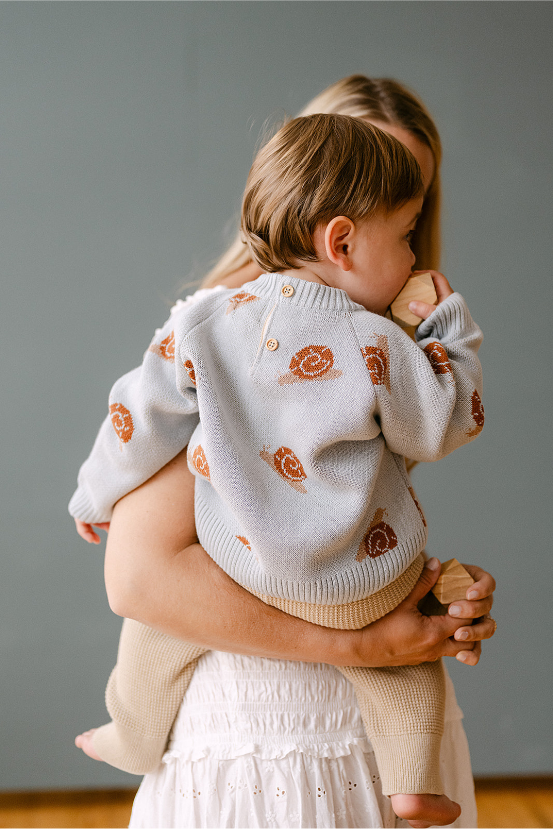 Image shows baby boy wearing organic cotton knit sweater with jacquard snail pattern in pearl blue. 