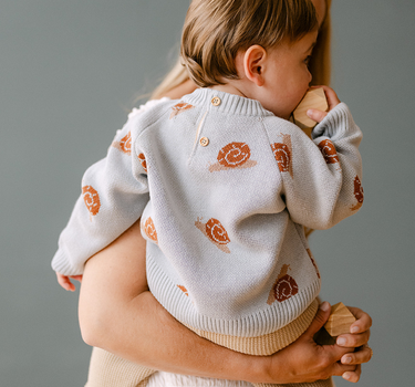 Image shows baby boy wearing organic cotton knit sweater with jacquard snail pattern in pearl blue. 