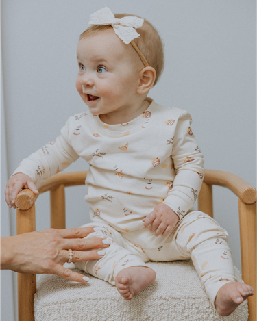 Baby wearing modal pajama set in Petit Déjeuner print with coffee mugs, croissants, butter, and jam.