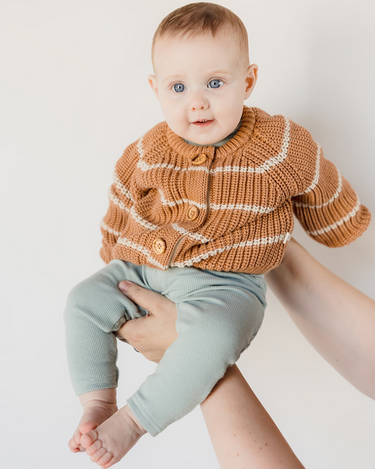 Picture shows baby girl in mom's arms wearing organic cotton knit cardigan with acorn and cream stripes and Magnetic Buttons. 