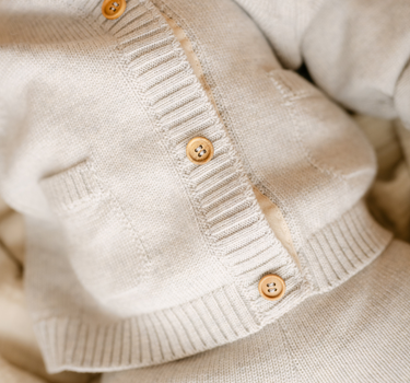 Image shows baby girl wearing merino wool baby cardigan in light heather gray. 