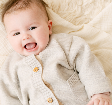 Image shows baby girl wearing merino wool baby cardigan in light heather gray. 