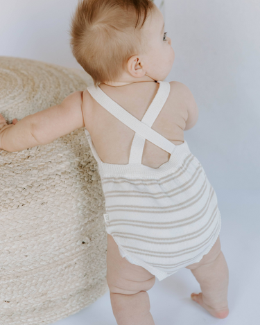 Baby girl standing wearing organic cotton knit romper in mushroom stripes. 
