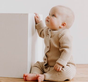 Photo shows baby girl sitting wearing sandcastle organic cotton knit romper with Magnetic Buttons.