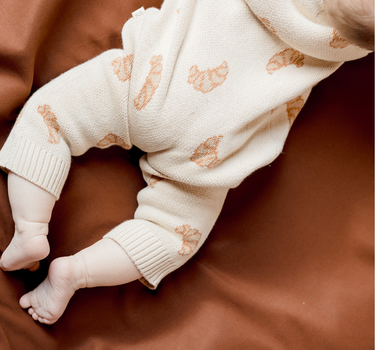 Baby laying on belly wearing organic cotton knit romper with croissant jacquard and Magnetic Buttons from neck to crotch.