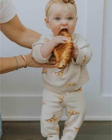 Baby wearing organic cotton knit croissant patterned joggers and matching sweater.