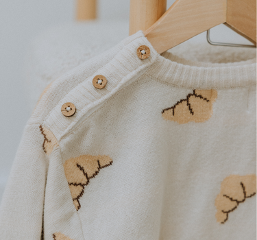 Organic cotton knit croissant patterned sweater with Magnetic Button closures at the neck hanging on hanger.