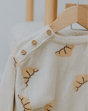 Organic cotton knit croissant patterned sweater with Magnetic Button closures at the neck hanging on hanger.