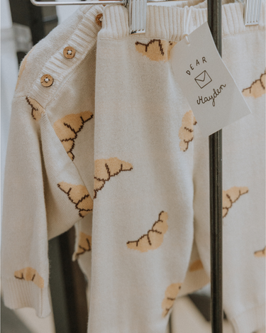  Organic cotton knit croissant patterned joggers and matching sweater hanging from hangers.