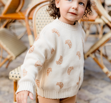 Image shows little girl wearing organic cotton knit croissant sweater with organic cotton modal rib leggings in acorn.