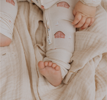 picture of baby boy wearing modal convertible footy pajamas in light beige color with farm print