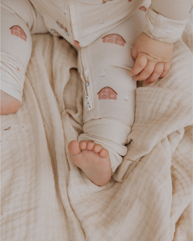 picture of baby boy wearing modal convertible footy pajamas in light beige color with farm print