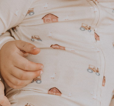 picture of baby boy wearing modal convertible footy pajamas in light beige color with farm print