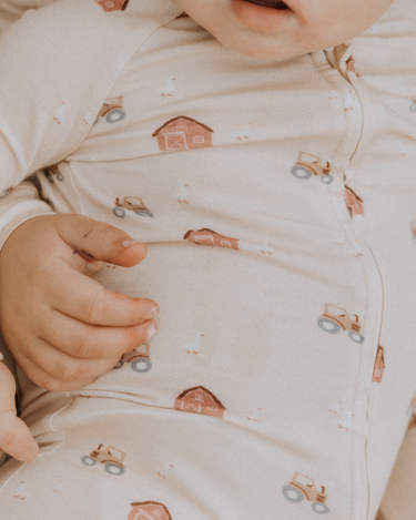 picture of baby boy wearing modal convertible footy pajamas in light beige color with farm print