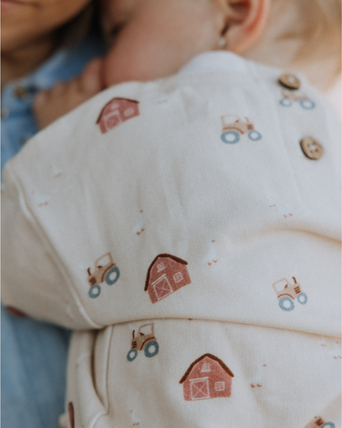 baby wearing organic cotton fleece sweatshirt in beige color with farm print and magnetic closures at the back of the neck