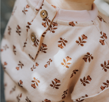 image of baby girl wearing organic cotton pink floral rose sweatshirt with magnetic buttons at the back of the neck