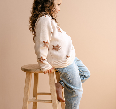 Image shows little girl wearing organic cotton knit sweater with jacquard fox pattern in pale pink. 