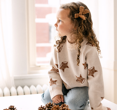 Image shows little girl wearing organic cotton knit sweater with jacquard fox pattern in pale pink. 