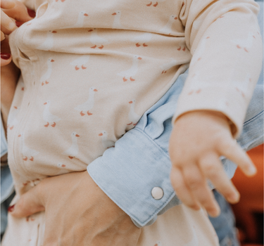 Baby wearing an organic cotton modal playsuit in geese pattern.