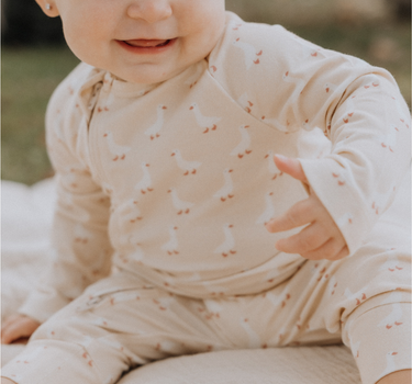 Baby wearing an organic cotton modal playsuit in geese pattern.