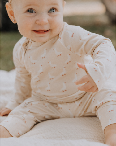 Baby wearing an organic cotton modal playsuit in geese pattern.